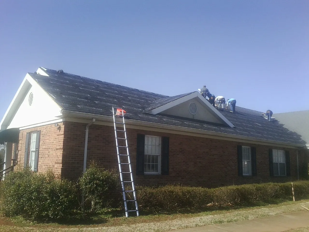 Crew tearing shingles off a brick ranch roof with a ladder set — Metal Roof Repair work by our crew in Kensington