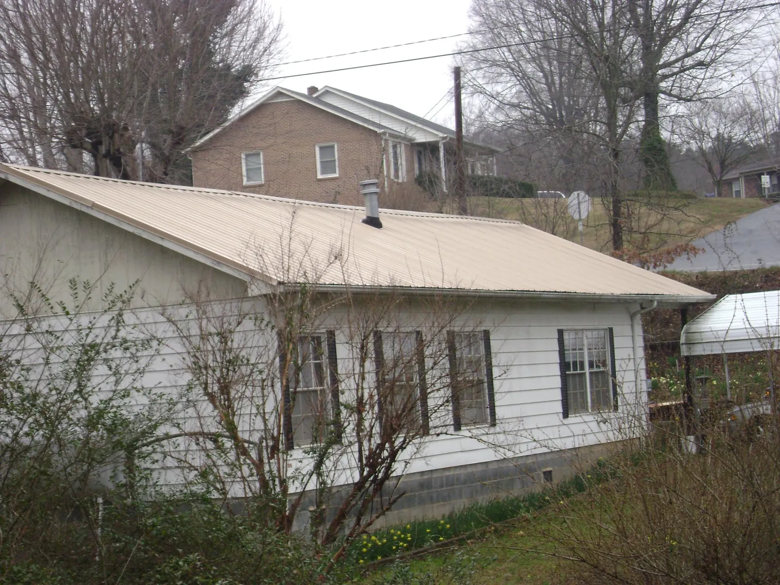 Tan metal roof on a white sided house set into a hillside — Commercial Roofing by Roofing Brothers in Kensington